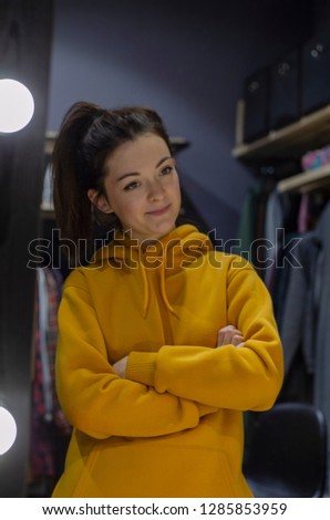 lifestyle fashion portrait of young stylish hipster woman in womens store showroom, standing near clothes rack indoors. Stylish wardrobe, wearing cute trendy outfit