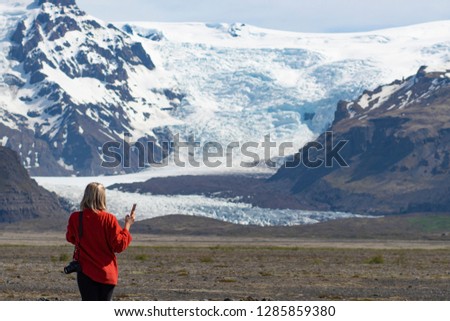 Young woman taking a picture of snow mountain at Skaftafell Glacier (Svínafellsjökull) National Park in South Iceland during Summer with Blue Sky