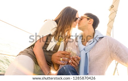 Rich young couple in love on sailboat kissing at sunset - Luxury lifestyle concept sailing around world - Soft focus on warm sunshine filter - Lens flare and tilted horizon as part of composition