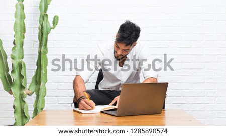 Arabic young man with laptop writing in a notebook