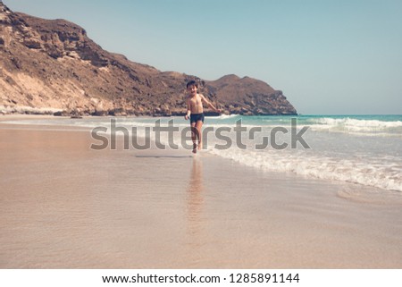 full length of boy running on the beach and having fun on sunny day