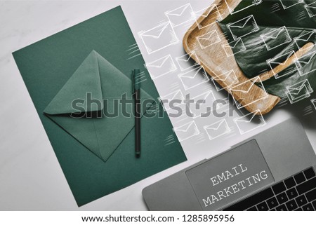 Green paper for letter template by laptop on white marble background with email marketing and icons