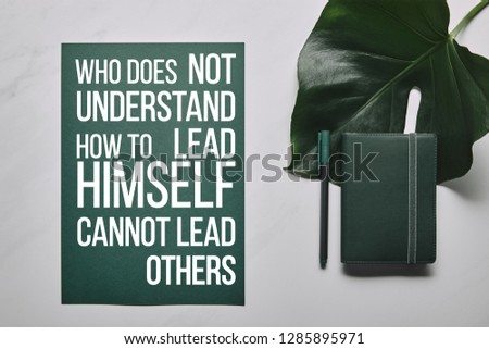 Green stationery set and monstera leaf on white marble background with "who does not understand how to lead himself cannot lead others" lettering  
