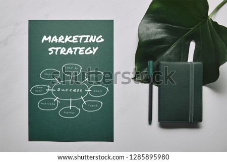 Green stationery set and monstera leaf on white marble background with marketing strategy icons