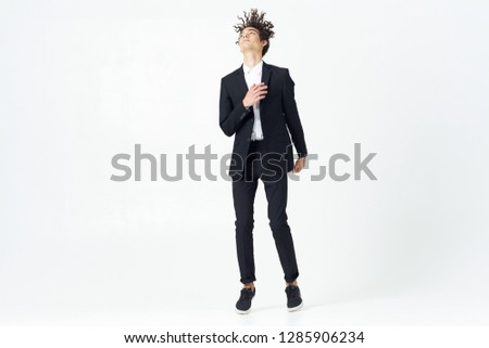 Curly-haired man in a dark suit in full growth on a light background standing on his socks