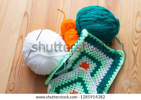 balls of green, orange and white yarn lie on a wooden table next to the finished product.