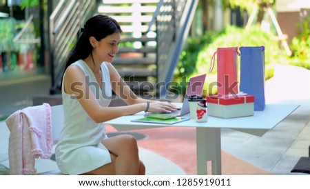 The pretty woman was happiness while using laptop, She use hand typing and smiling, a present box and shopping bags placed on table