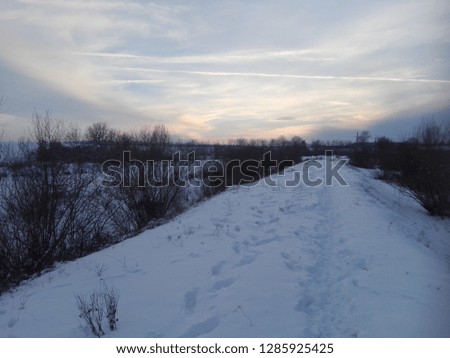 winter sunset over a snowy road near a river shore