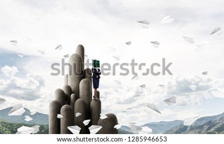 Business woman in suit with monitor instead of head keeping arms crossed while standing on the top of stone columns among flying paper planes with beautiful landscape on background. 3D rendering.