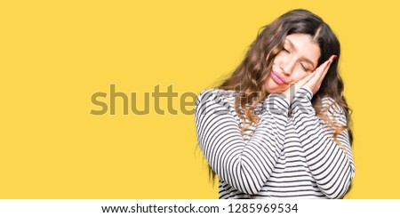 Young beautiful woman wearing stripes sweater sleeping tired dreaming and posing with hands together while smiling with closed eyes.