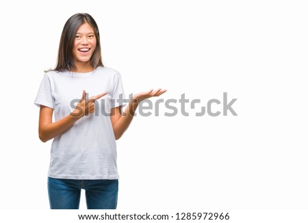 Young asian woman over isolated background amazed and smiling to the camera while presenting with hand and pointing with finger.