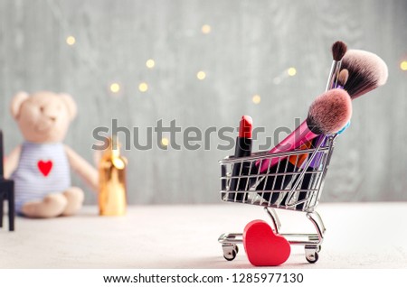Creative holiday image. Cart with lipstick, make-up brushes, tiny heart symbol, perfume and fairy-lights on a background. St Valentine's day concept Royalty-Free Stock Photo #1285977130