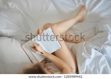 Close up lifestyle soft image of pretty young woman sitting on her cozy bed and making notes to her diary. Fall season mood. Bright colors.