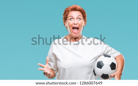 Atrractive senior caucasian redhead woman holding soccer ball over isolated background very happy and excited, winner expression celebrating victory screaming with big smile and raised hands