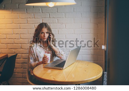 Picture of beautiful young woman smilling infront of computer in a cafe and talking by the phone