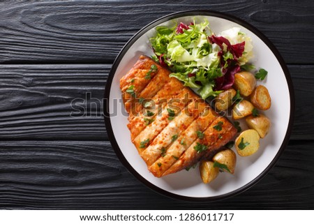 Healthy lunch grilled swordfish fillet with fried potatoes and fresh salad close-up on a plate on a wooden table. horizontal top view from above Royalty-Free Stock Photo #1286011717