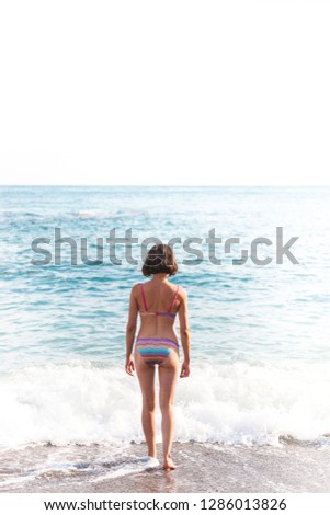 The girl goes into the sea water. Woman bathes in the ocean. Rest on the coast. Slender brunette in a swimsuit is on the beach.