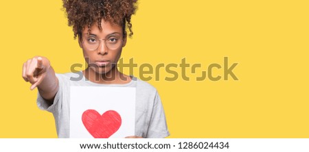 Young african american woman holding paper with red heart over isolated background pointing with finger to the camera and to you, hand sign, positive and confident gesture from the front