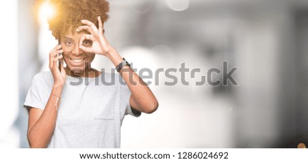 Young african american woman talking on smartphone over isolated background with happy face smiling doing ok sign with hand on eye looking through fingers