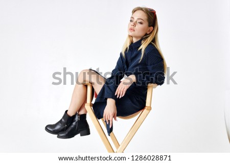   fashionable woman in glasses in a dress sits on a chair on a light background                             