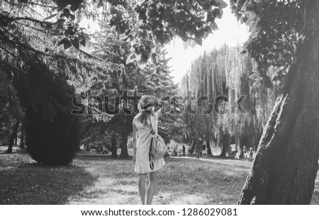 Stylish hipster girl with a straw hat  is standing outdoors. Woman in blue dress. Silver grey backpack. Travel holiday concept. Summer lifestyle photo. Shades of sun and trees.