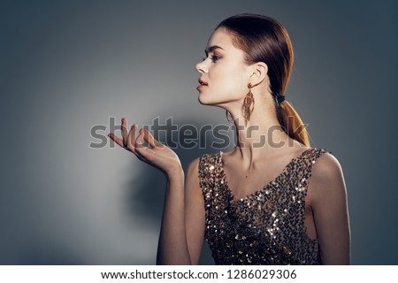 beautiful glamor woman wearing gold dress and earrings holds hand near face