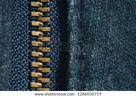 Macro of yellow zipper on blue jeans trousers, selective focus zipper. Royalty high-quality free stock photo image of close up of gold zipper on a blue jean trousers background with space for text

