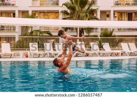 a man raises a child in the pool. Tanned happy father and son on vacation