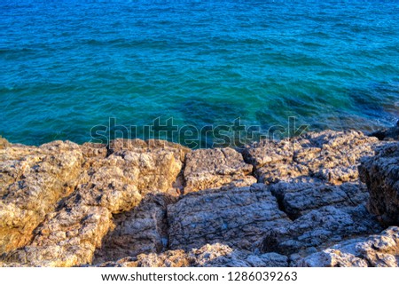 View from the rock on the beautiful blue sea near the Salou, Spain, Catalonia. Sunny day near to the Mediterranean sea, waves break by coast rocks. Sea rocks with salt deposits. Green and blue water