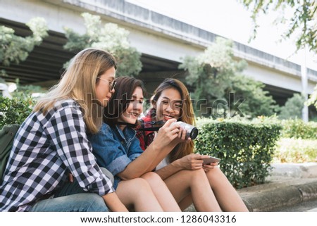 Group of Asian women sitting together and looking checking photo while traveling at park in urban city in Bangkok, Thailand. Lifestyle friends tourist travel holiday in Thailand concept.