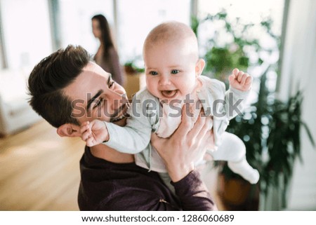 A portrait of young father with a baby girl standing indoors in a room.