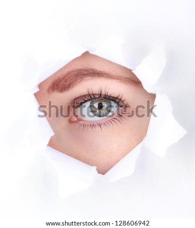 Female eye looking through hole in sheet of paper