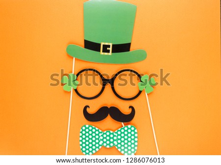 Creative st Patricks Day orange background. Flat lay composition of Irish holiday celebration with photo booth decor: hat, glasses, bow tie, lips. With Copy space, greeting card, top view