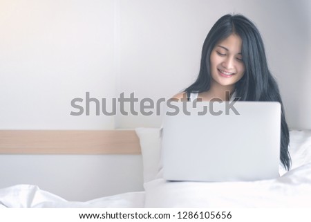 Young woman working on a laptop sitting on bed at home.