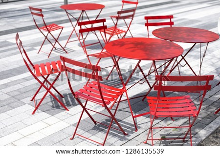 Background of red metal patio furniture, with chairs and tables in a bright courtyard