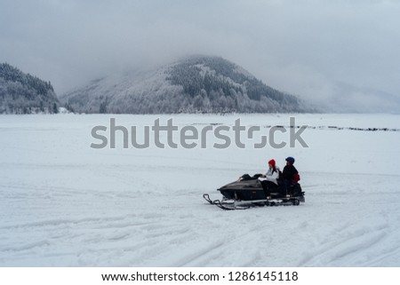 Side view of man and woman riding fast on a snowmobile on the frozen lake in the mountains with the scenic view.