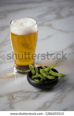 Portion Japanese Edamame soy beans in porcelain bowl with beer glass on marble background