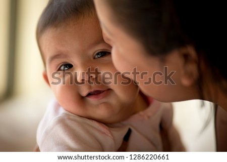 Young mother kisses her smiling baby daughter on the cheek.