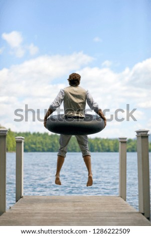 Man with inner tube around him, jumping off a jetty into a lake.