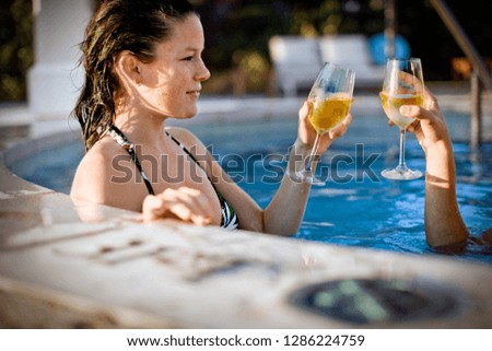 Woman toasting with her friend in a swimming pool