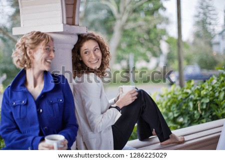 Two women sitting on a porch drinking coffee and smiling