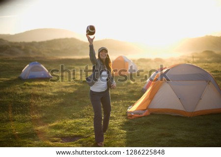 Portrait of a laughing young woman throwing a football in a campsite at sunset.