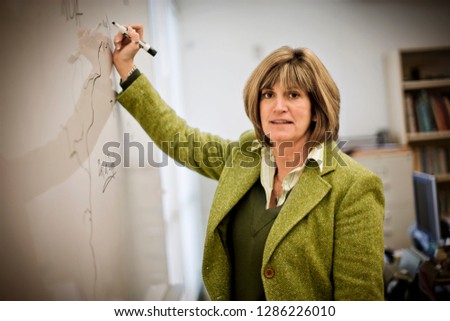 Portrait of a mid-adult female teacher writing in a whiteboard in a school.