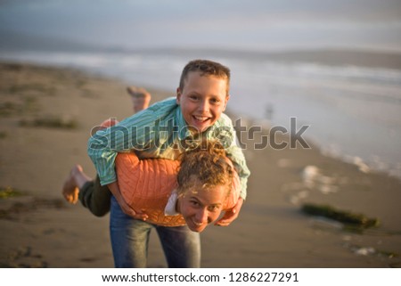 Portrait of a smiling teenage girl and her younger brother giving each other a piggyback on the beach.