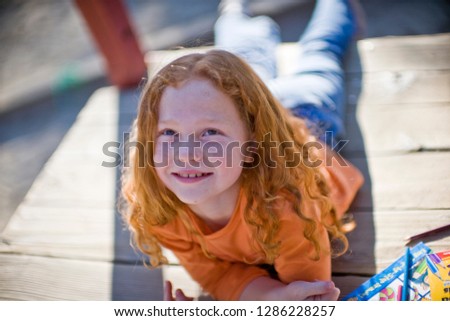 Smiling young girl lying on her front on a wooden platform outside in the sun.