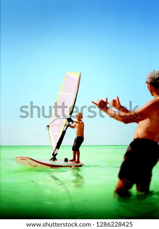 Man teaching a boy how to windsurf in the sea.