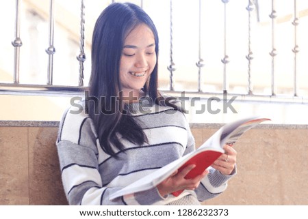 The image of a teenage student who is committed to studying with a book under a sweet smile.