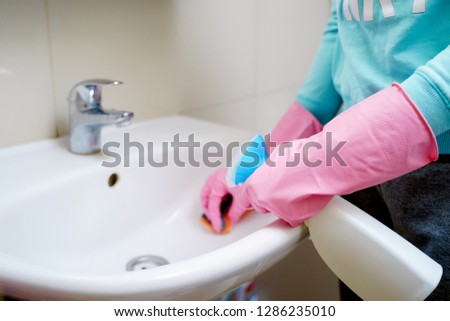 Picture of female hands in rubber gloves washing sink in bath