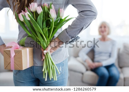 Happy Mother's day. Woman hiding flowers and gift box for her mature mother