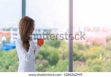 Business woman in white is holding a red coffee cup by the windows